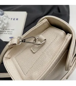 Détail de la texture cuir litchi crème et ferrures en argent poli sur le sac bandoulière