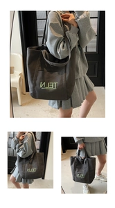 Detail view of large dark grey canvas tote bag with green embroidered lettering