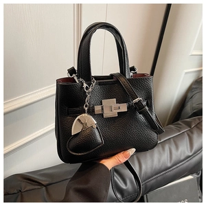Detail of black lychee grain leather handbag with heart charm and gold twist lock closure