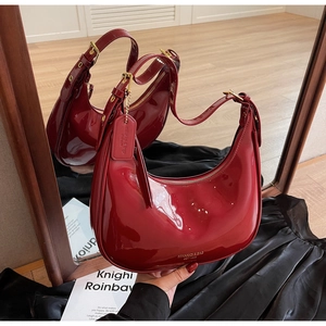Detailed macro view of glossy red patent leather hobo bag with gold metal zipper and logo