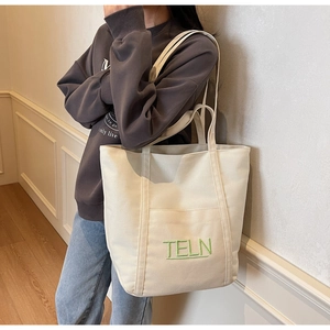 Detail of off-white canvas tote bag featuring green TELN embroidery and wide handles