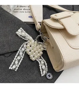 Détail d'un pendentif cœur en perles blanches avec nœud sur un sac beige texturé