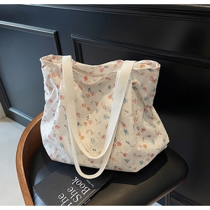Detail einer weißen Stofftasche mit floralem Muster auf einem schwarzen Ledersessel