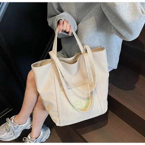 Detail of beige canvas tote bag with vibrant green TELN letter embroidery and sturdy handles