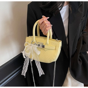 Detail shot of pale yellow leather bucket bag with lace bow and elegant pearl charm