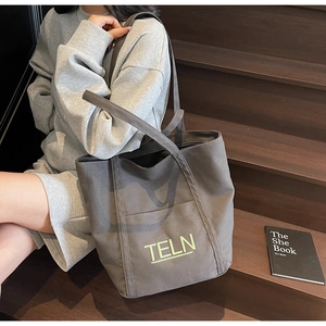 Detail of canvas tote bag with TELN green embroidery shown in a lifestyle casual setting