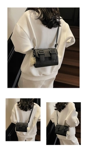 Detail of black pebbled leather crossbody bag with decorative buckles and pearl charm