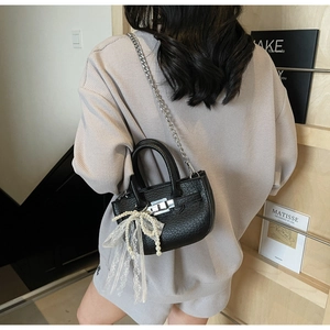 Detail of a black leather bucket bag with silver chain strap and pearl bow charm