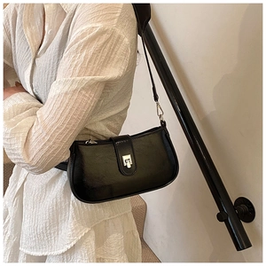 Detail of a black glossy faux leather underarm bag with silver buckle worn by a model