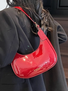 Glossy red patent leather crescent underarm bag shown on model with luxury finish