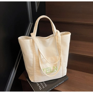Detailed close-up of beige canvas tote bag featuring green TELN embroidery and front pocket