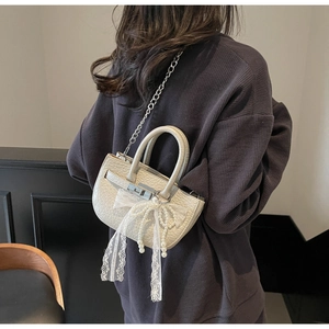 Detailed shot of cream bucket bag with lace bow, pearl charm and silver chain strap