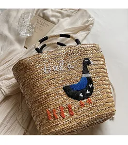 Detail of straw tote bag featuring duck embroidery and contrast woven handles on dress