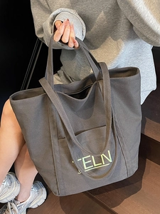 Deep grey canvas tote bag with embroidered letters, shown on a model in a casual setting