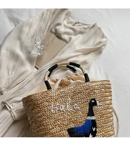 Detail showing handwoven straw beach bag with goose embroidery and rope handle