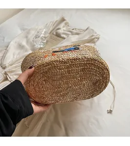 Detail view of woven straw beach bag featuring bird embroidery and thick oval base