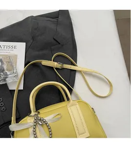 Detail of a bright yellow Boston bag with lychee texture leather and a pearl bow charm