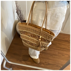 Detail view of woven straw tote bag with long handles and decorative wooden bead tassels