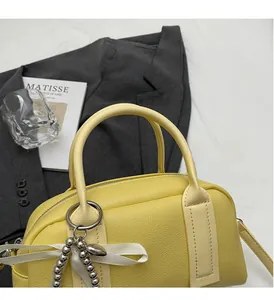 Detail of yellow lychee leather Boston bag featuring a silk bow and metal ring charm