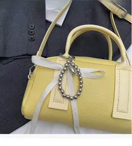 Detail of yellow lychee leather Boston bag with white ribbon and silver metal charm