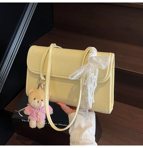 Dettaglio borsa beige in ecopelle con fiocco in pizzo e ciondolo orsetto