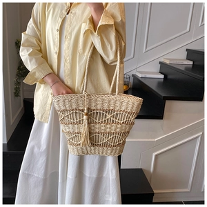 Detail of hand-woven straw tote bag with fringe tassel and hollow patterns on steps
