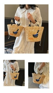 Detail view of woven straw beach bag featuring cute duck embroidery and black handles