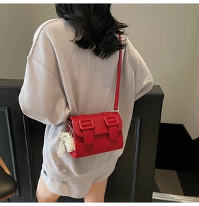 Detail of red textured leather crossbody bag with lace pearl pendant and buckle closure