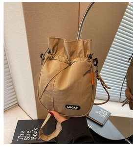 Detail view of khaki drawstring bucket bag with Lucky patch and orange side label detail