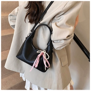 Close-up of black crescent handbag with decorative pearl chain and pink bow detail