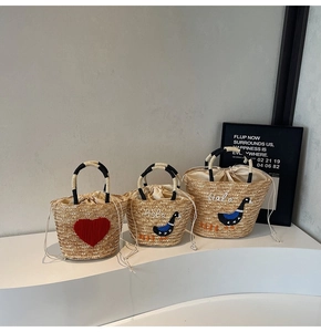 Detail view of woven straw tote bag set with heart embroidery and striped handles