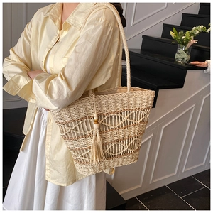 Close-up detail of bohemian straw tote bag featuring tassel charm and woven pattern