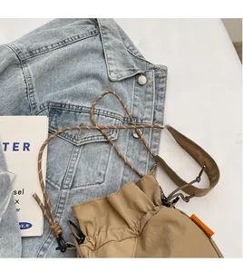Detail of khaki drawstring bucket bag with orange tag worn over a denim jacket