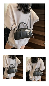Detail of black lychee texture Boston bag with pearl heart charm and white silk bow