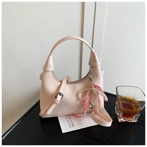 Detail of light pink oil wax leather crescent bag with decorative ribbon and bead charm