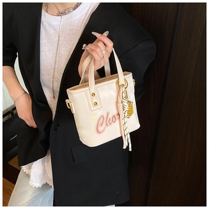 Détail d'un sac seau vernis blanc crème avec imprimé lettres rouges et breloque dorée