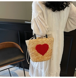 Macro shot of a straw beach bag featuring a red heart motif and drawstring inner pouch