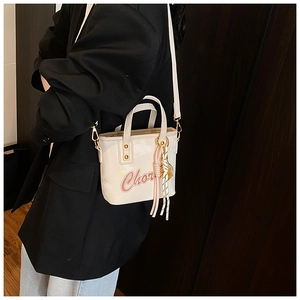 Détail du sac seau crème avec texte Chor rose et pompon en cuir sur un mannequin