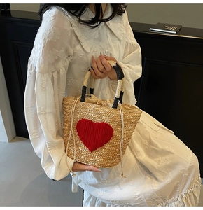 Detailed close-up of straw woven tote bag featuring a red heart pattern and rope handles
