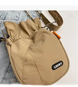 Close-up of khaki nylon drawstring bucket bag featuring black Lucky patch and orange webbing