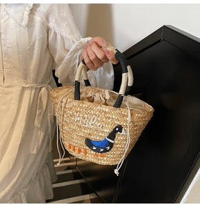 Detail of straw handbag featuring swan embroidery and black and white woven handles