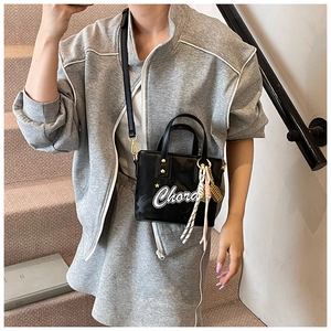 Détail du sac seau noir brillant avec imprimé Chora et breloque tissée sur une tenue