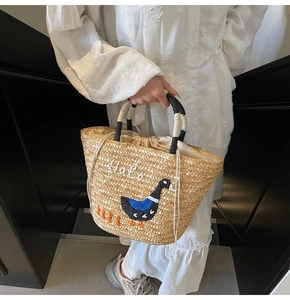 Detail of straw woven tote bag featuring Hola embroidery and swan design with drawstring liner