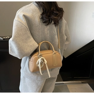 Chic beige Boston bag with pearl ribbon charm shown in a modern interior setting