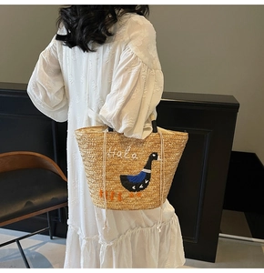 Detailed close-up of straw tote bag with cartoon duck embroidery and drawstring closure