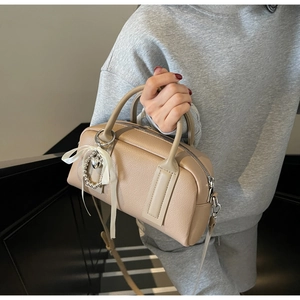 Detail of cream Boston bag with lychee grain leather, silk bow, and heart pearl charm
