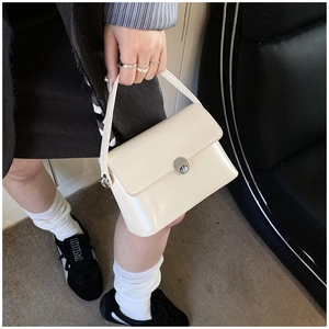 Detail of a creamy white oil wax leather handbag with a round metal twist lock closure