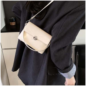 Close-up of cream square crossbody bag with silver twist lock on dark blazer
