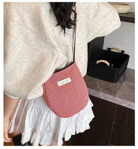 Detail of red gingham crossbody bag with branded woven label worn on person's back