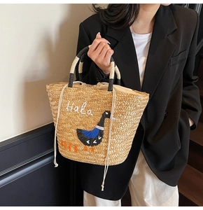 Detail of straw bag featuring bird embroidery, Halo text and drawstring closure